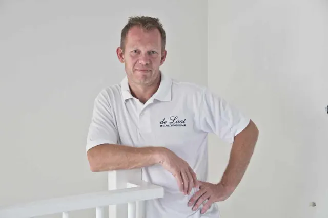 Portret van Hans de Laat in werkkleding met logo